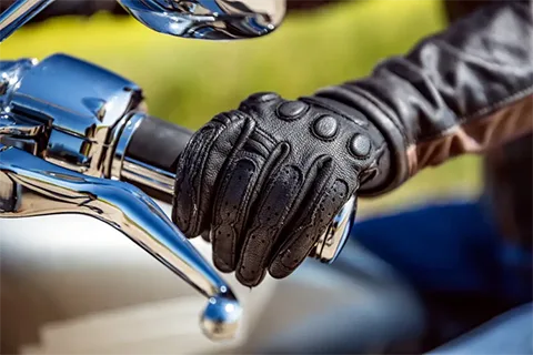Close-up of a gloved hand on a motorcycle handlebar with a blurred background