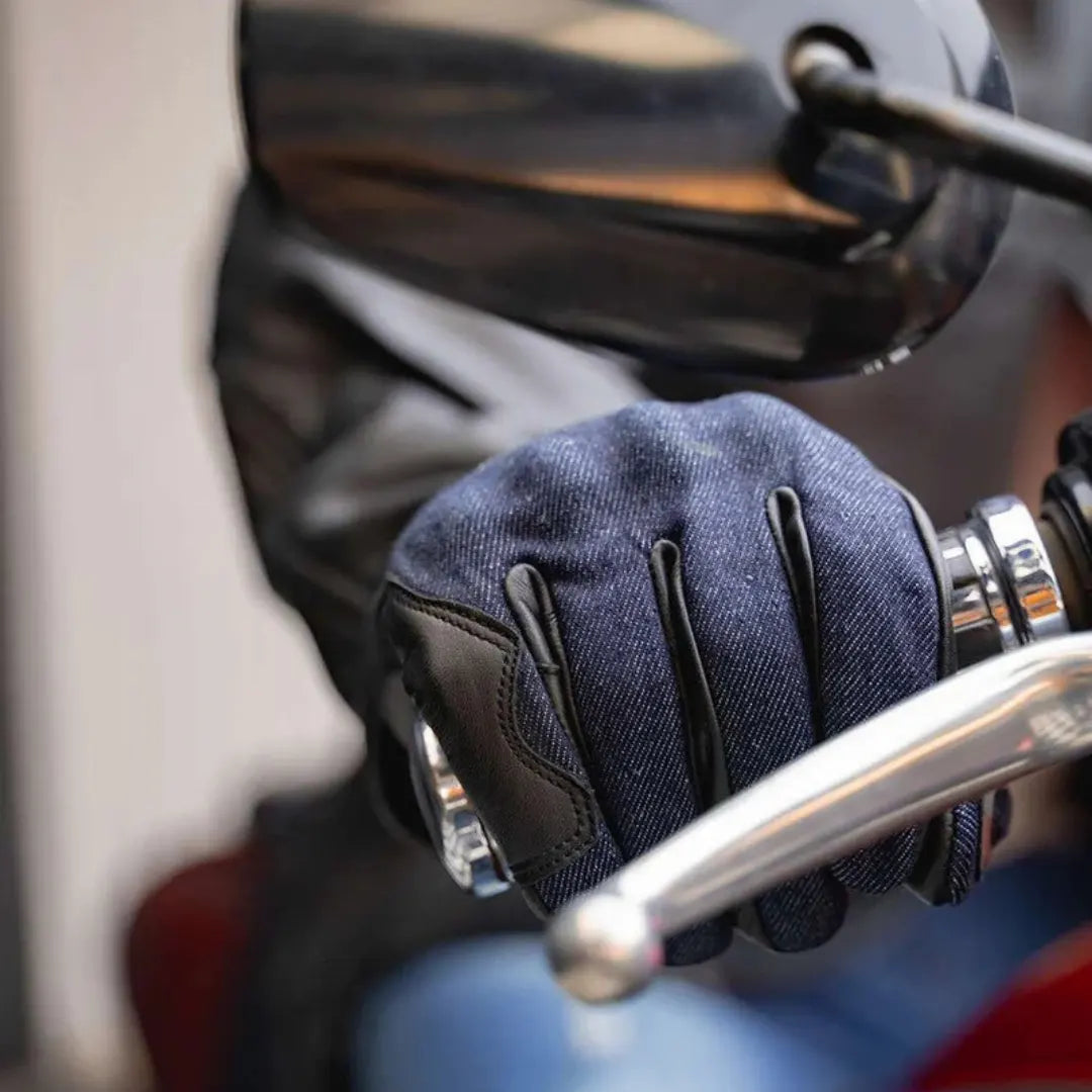 Leather motorcycle glove on hand, gripping a motorcycle handlebar with touchscreen functionality for mobile use