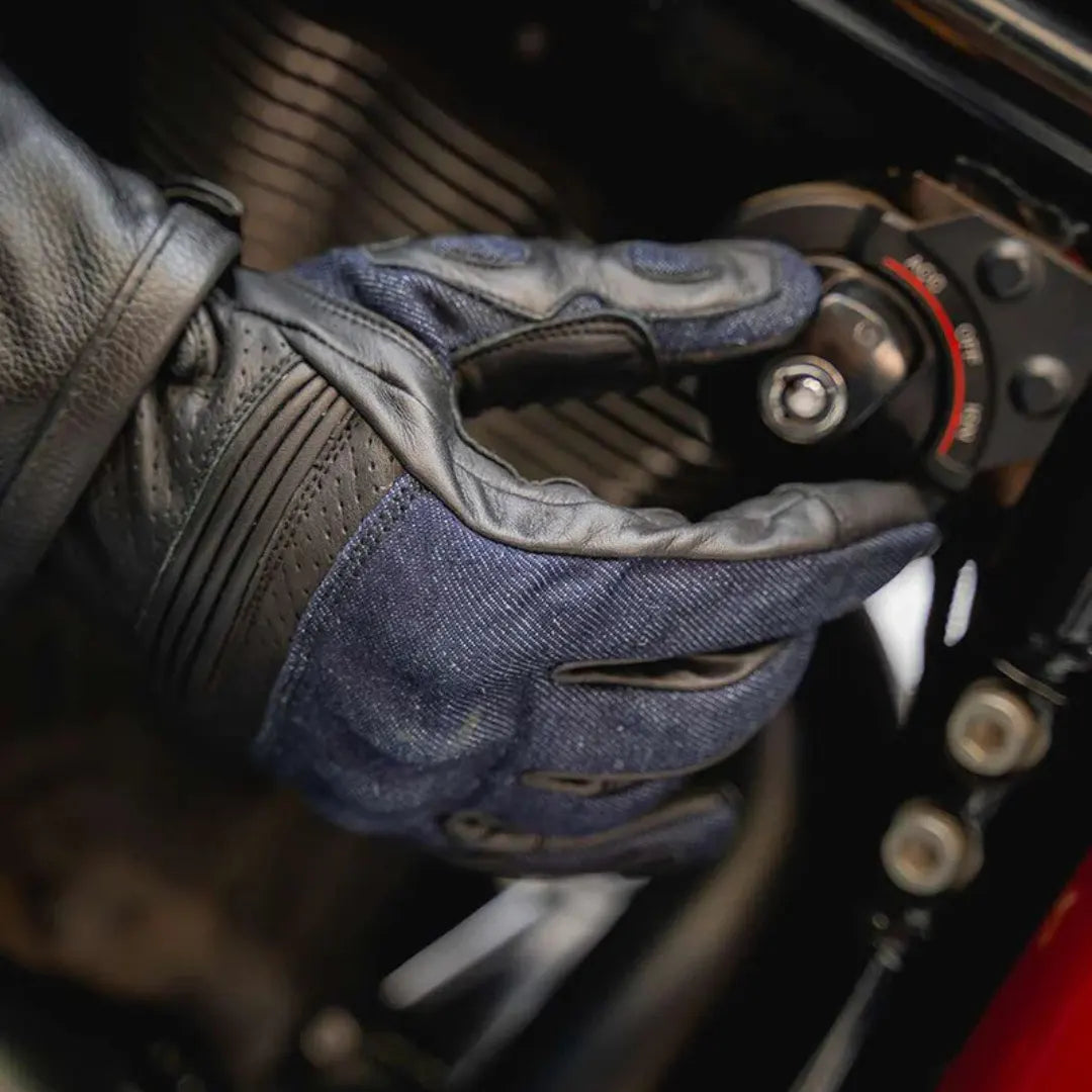 Black denim leather motorcycle glove in use, adjusting motorcycle components with touchscreen sensitivity for easy mobile access