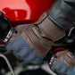 Leather motorcycle glove in use, adjusting motorcycle components with mobile phone touchscreen functionality.